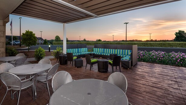 Een terras buiten met een overdekte zithoek, tafels en stoelen.