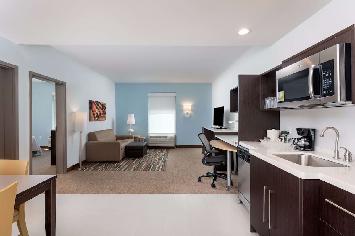 Een moderne hotelkamer met een kitchenette, een eethoek, een bank en een groot raam.