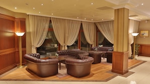 A spacious lobby with leather sofas, a floor lamp, and large windows with curtains. - Marina Residence Boutique hotel (Varna)