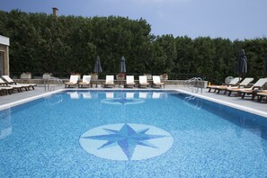 Una piscina con un diseño de mosaicos de estrellas, rodeada de sillones de descanso y sombrillas.