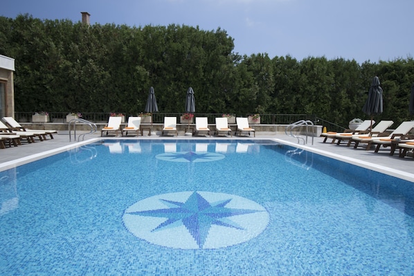 Ein Swimmingpool mit Sternen-Mosaikmuster, umgeben von Liegestühlen und Sonnenschirmen.