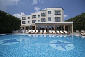 Una piscina con sillas de descanso y un edificio con varios balcones al fondo.
