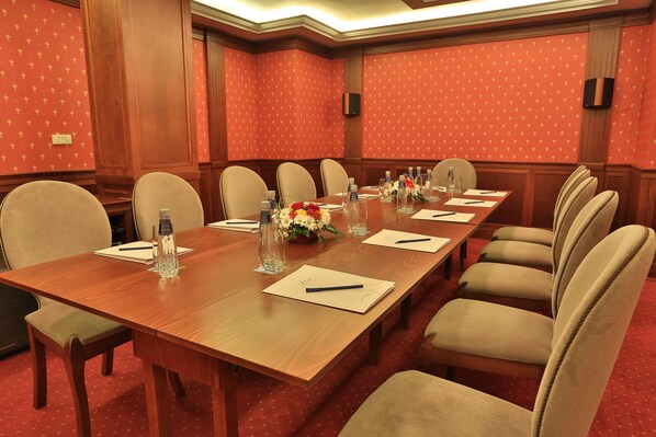 A conference room with a long wooden table, beige chairs, water bottles, and floral centerpieces.