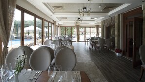 A spacious dining area with large windows, elegant chandeliers, and neatly arranged tables and chairs. - Marina Residence Boutique hotel (Varna)