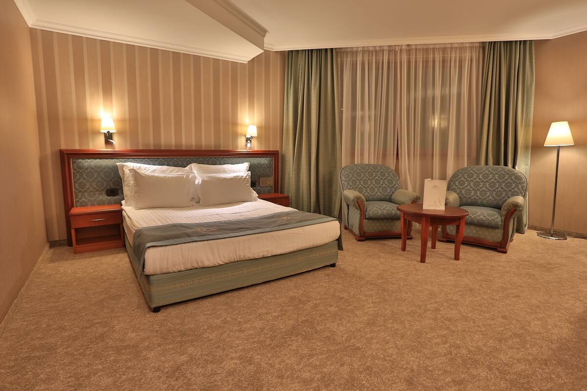 Una habitación de hotel con una cama grande, dos sillones, una mesita y una lámpara.