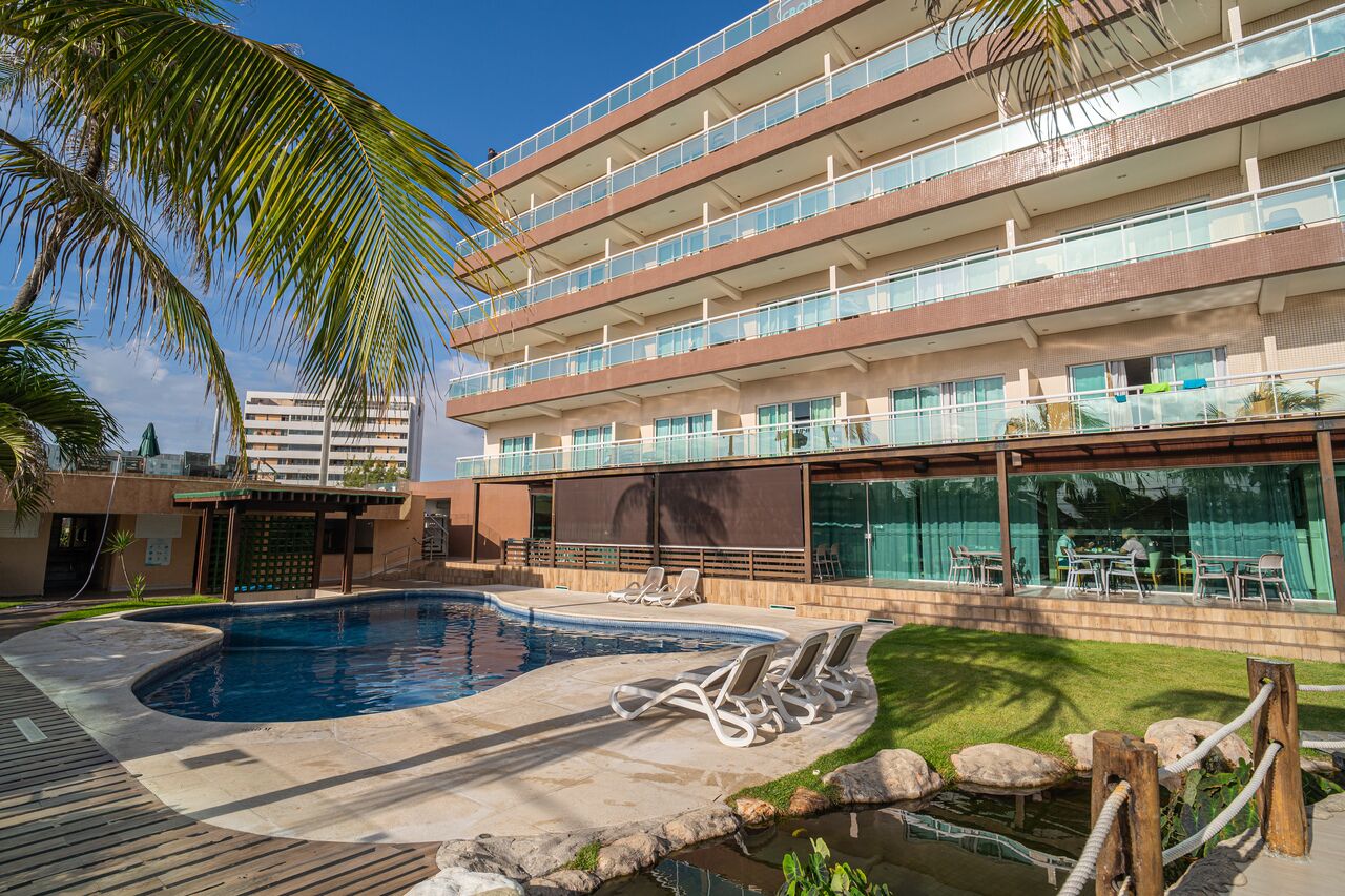 A hotel with a swimming pool, outdoor seating, and a multi-story building with balconies.