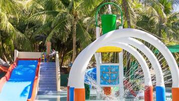 A water park with a blue slide, a water play area, and palm trees in the background.