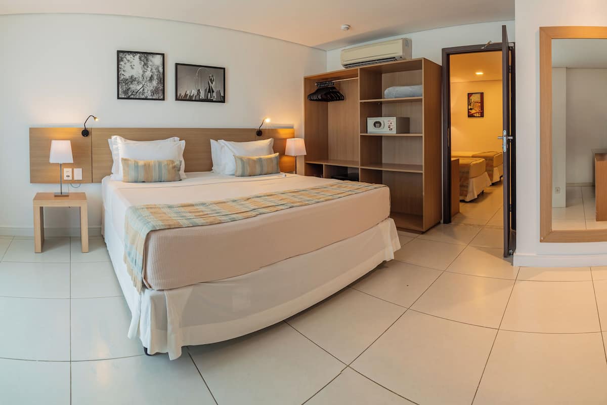 A modern hotel room with a large bed, bedside tables with lamps, a wardrobe, and a mirror.