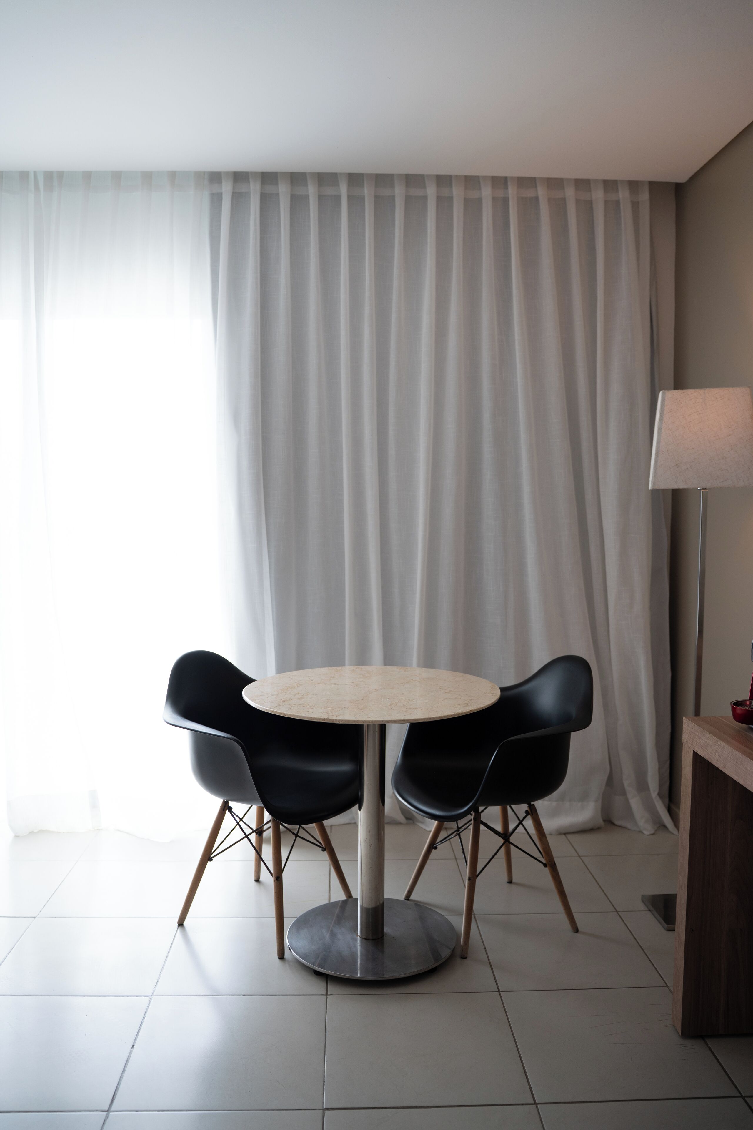 Et moderne spiseområde med et rundt bord, fire sorte stole, en lampe og en gardinbaggrund.