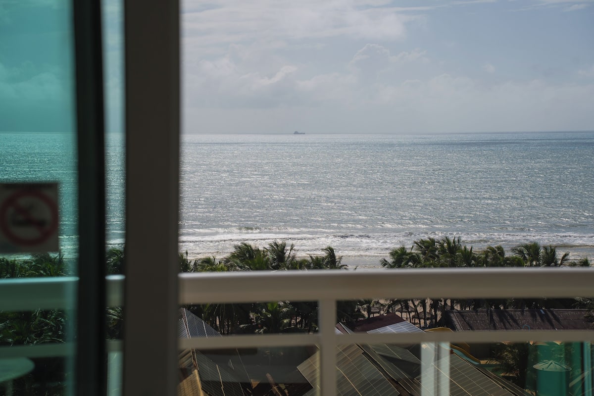 A view of the ocean from a balcony with a ship in the distance, palm trees, and a no-smoking sign.