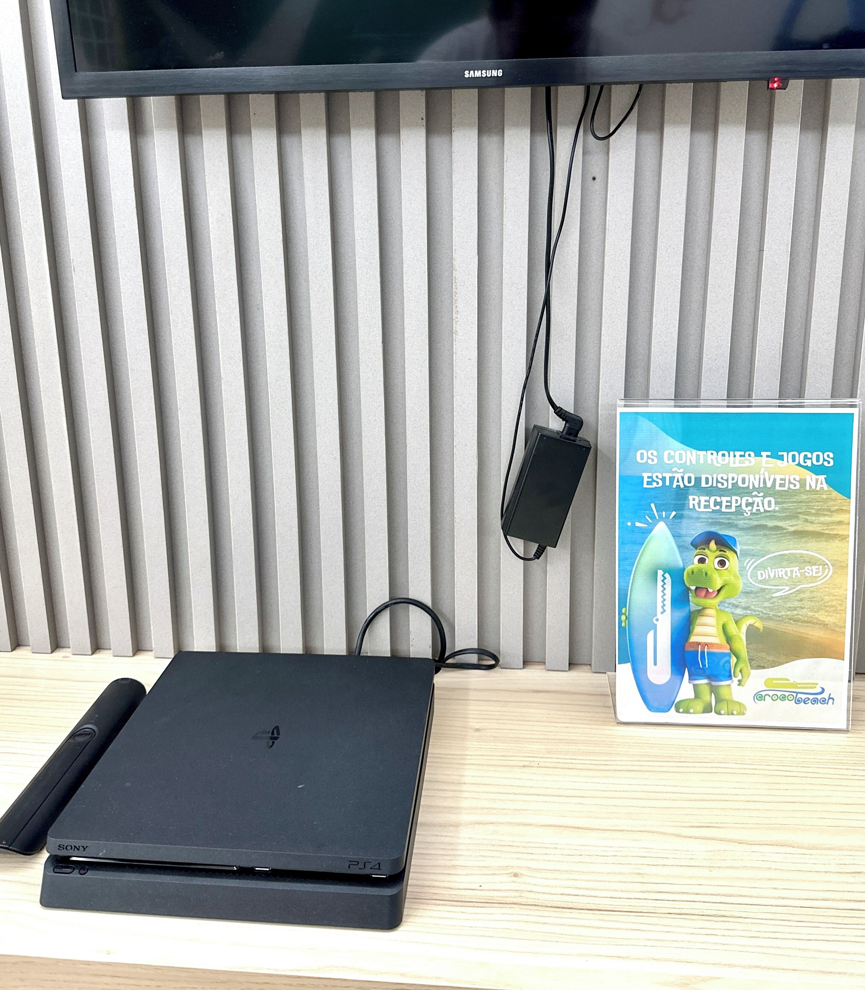 Una laptop Sony sobre un escritorio de madera, con un televisor montado en una pared con persianas verticales.