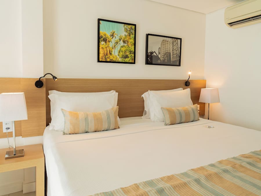 A hotel room with a large bed, two wall-mounted lamps, and two framed pictures on the wall.