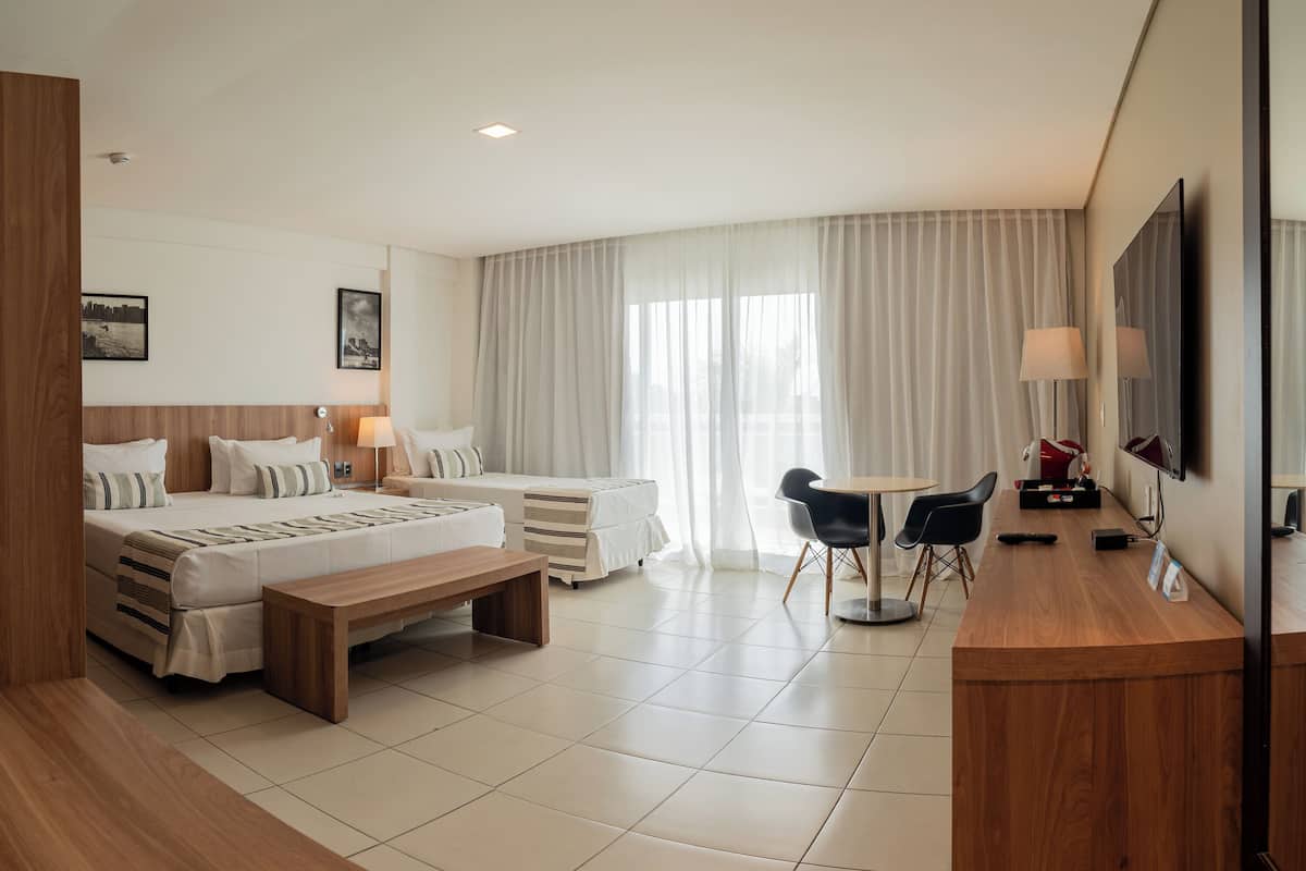 A hotel room with two beds, a desk, chairs, a TV, and a window with curtains.