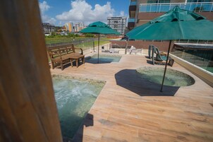 Zona de piscina en la azotea con bancos de madera, sombrillas verdes y vistas panorámicas de la ciudad.