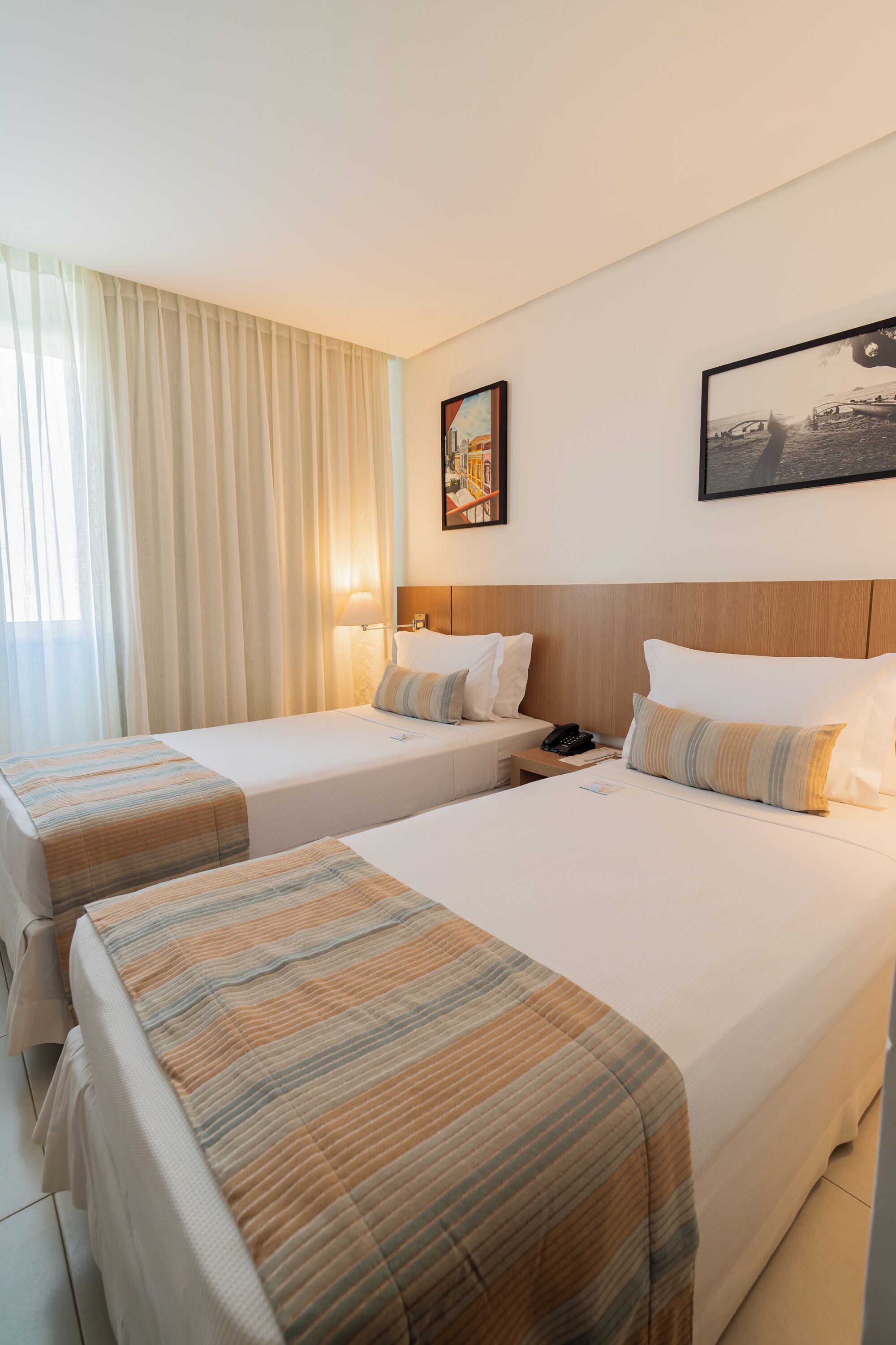 A hotel room with two beds, a nightstand, a lamp, and a painting on the wall.