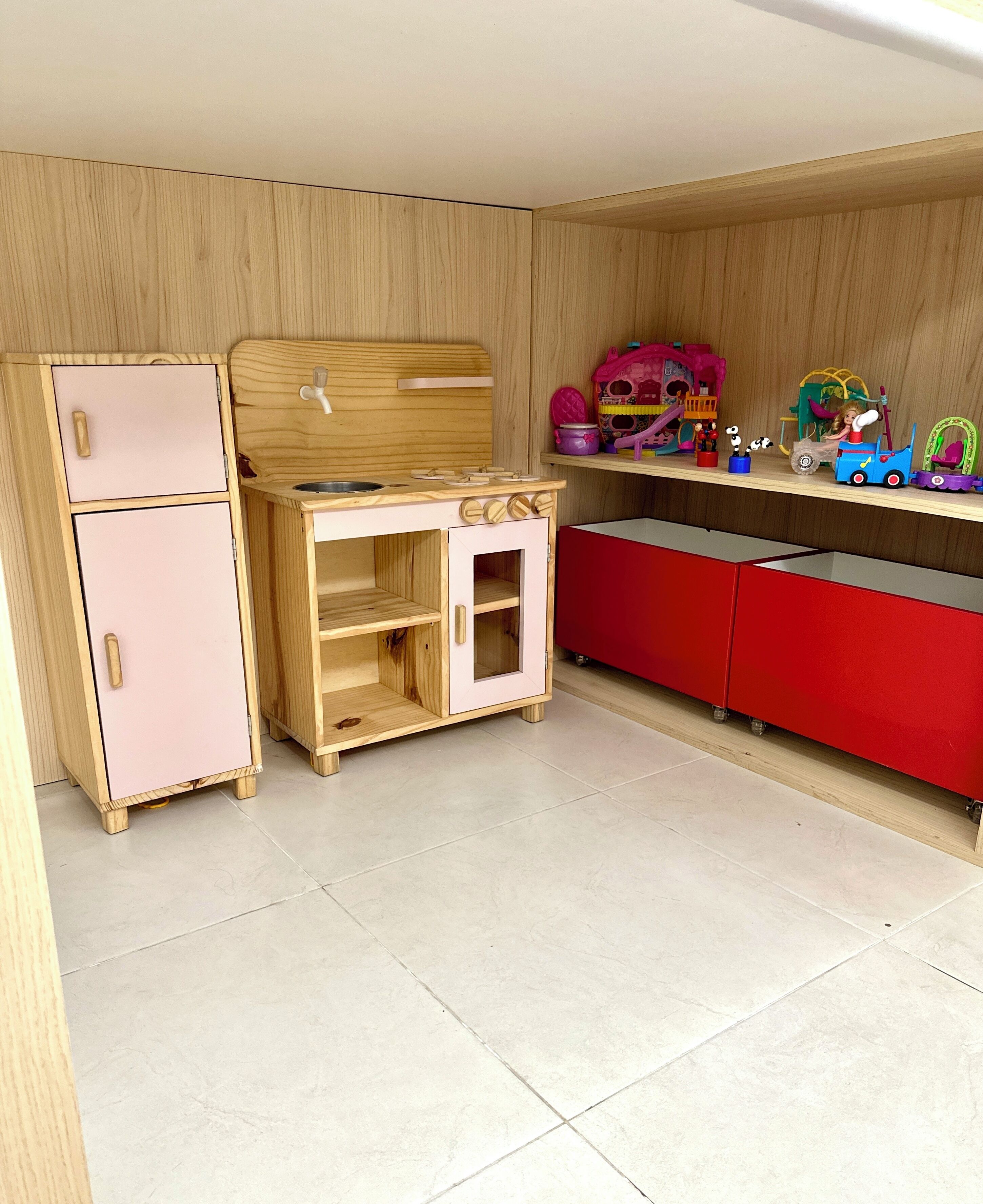 A children's play kitchen with a refrigerator, stove, and cabinets.