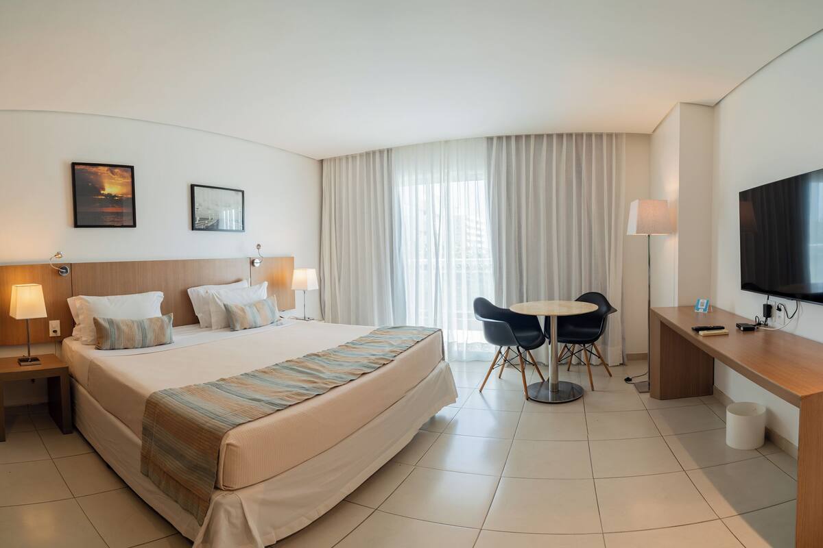 A hotel room with a large bed, a desk with a TV, a chair, and a table.