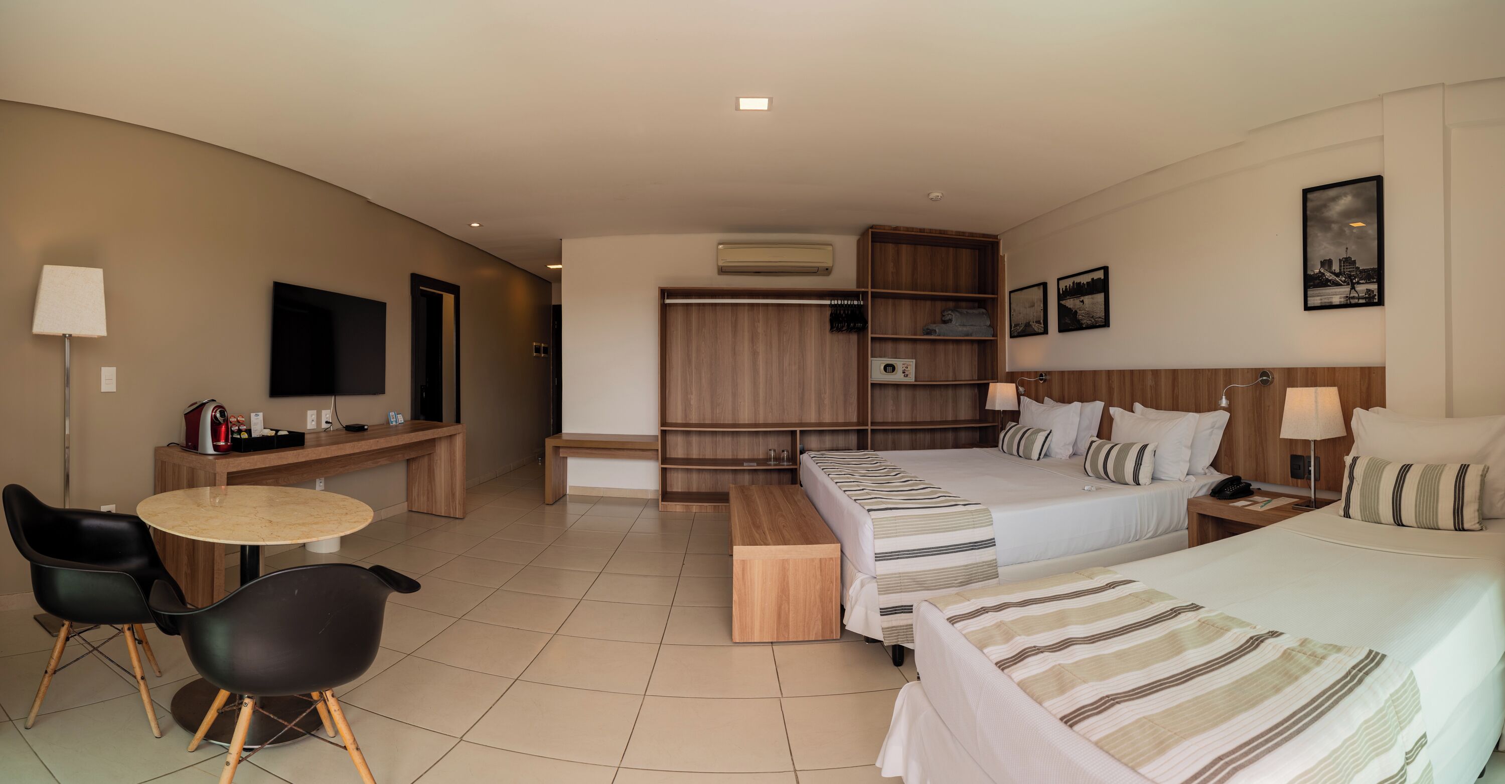 A hotel room with a bed, bedside tables, a desk, chairs, a TV, and a wardrobe.