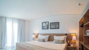 Quarto de hotel com uma cama grande, duas mesinhas de cabeceira, um guarda-roupa e duas luminárias fixadas na parede.