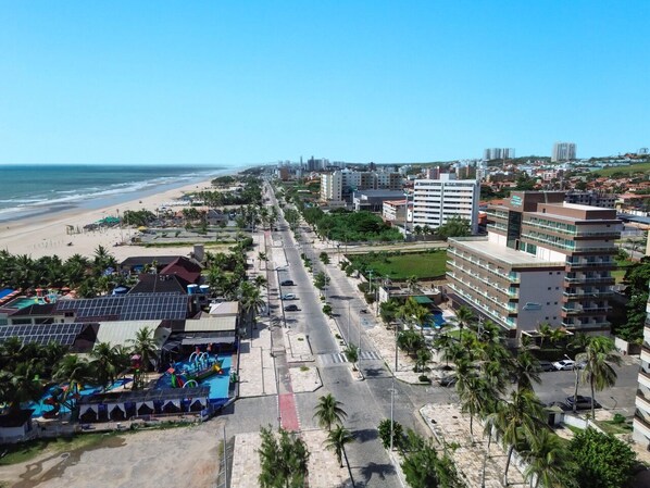 Un paysage urbain côtier avec une plage, une longue route bordée de palmiers et des bâtiments modernes.