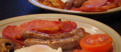 Two plates of breakfast food including sausages, eggs, tomatoes, and ham.