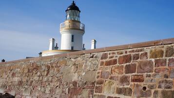 A lighthouse with a white cylindrical structure and a black top, situated next to a stone wall.