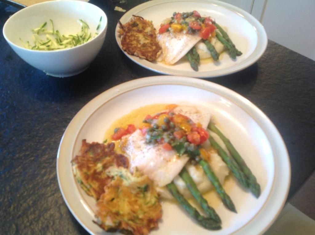 Two plates with food, one containing a fish fillet and asparagus, and the other with a potato dish and vegetables.