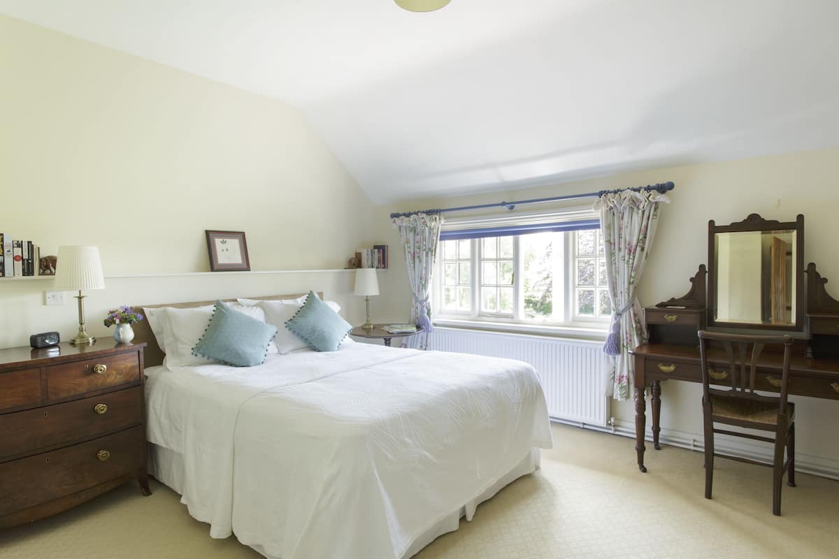 A bedroom with a large bed, a dresser, a mirror, and a window with curtains.