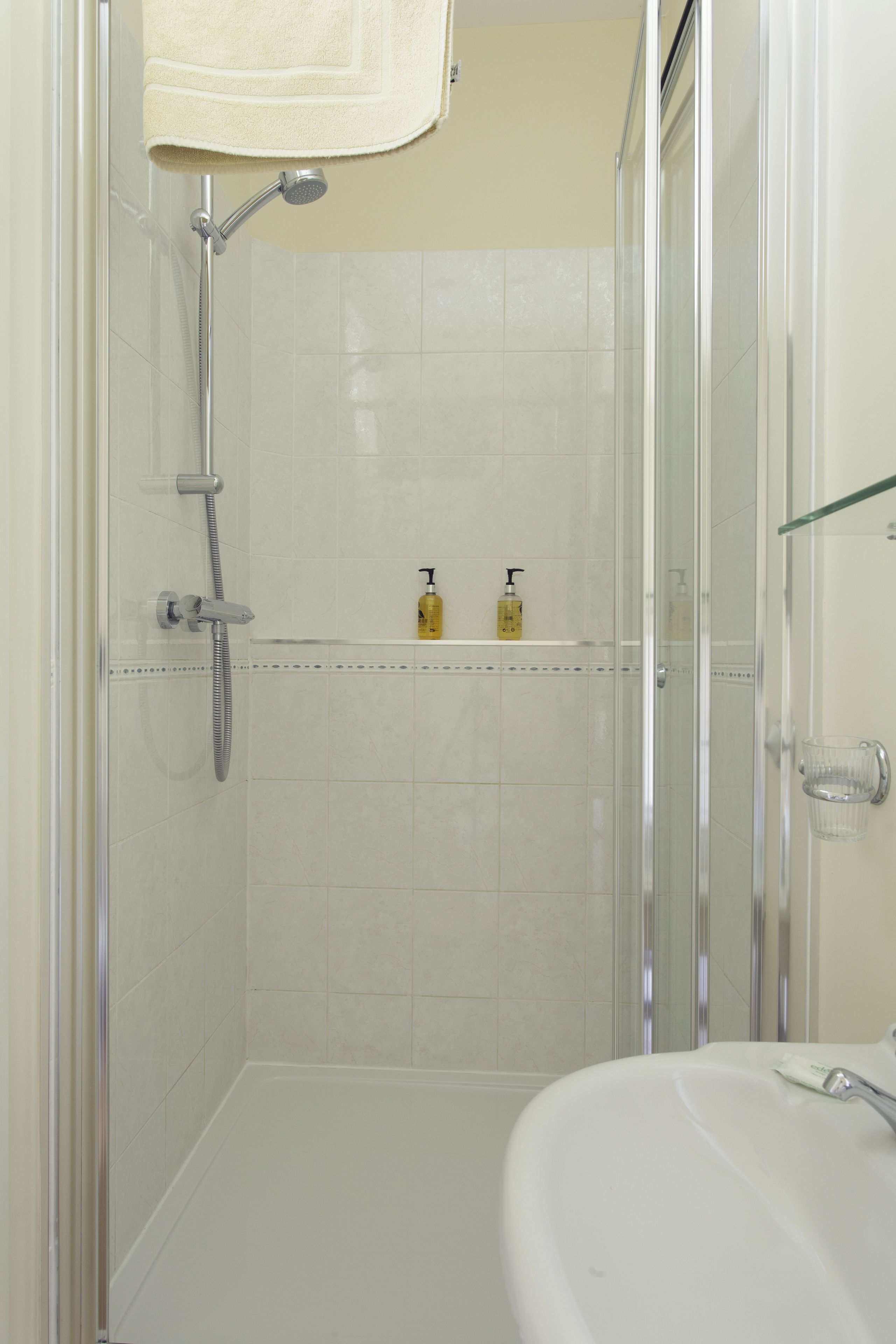 A bathroom with a shower, a sink, and a glass shelf with toiletries.