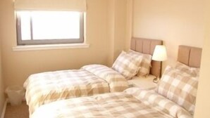 A bedroom with two beds, a window, and a nightstand with a lamp. - Marine View (Dundee)