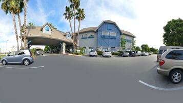 A hotel with a covered entrance, multiple cars parked in the lot, and palm trees in the background.