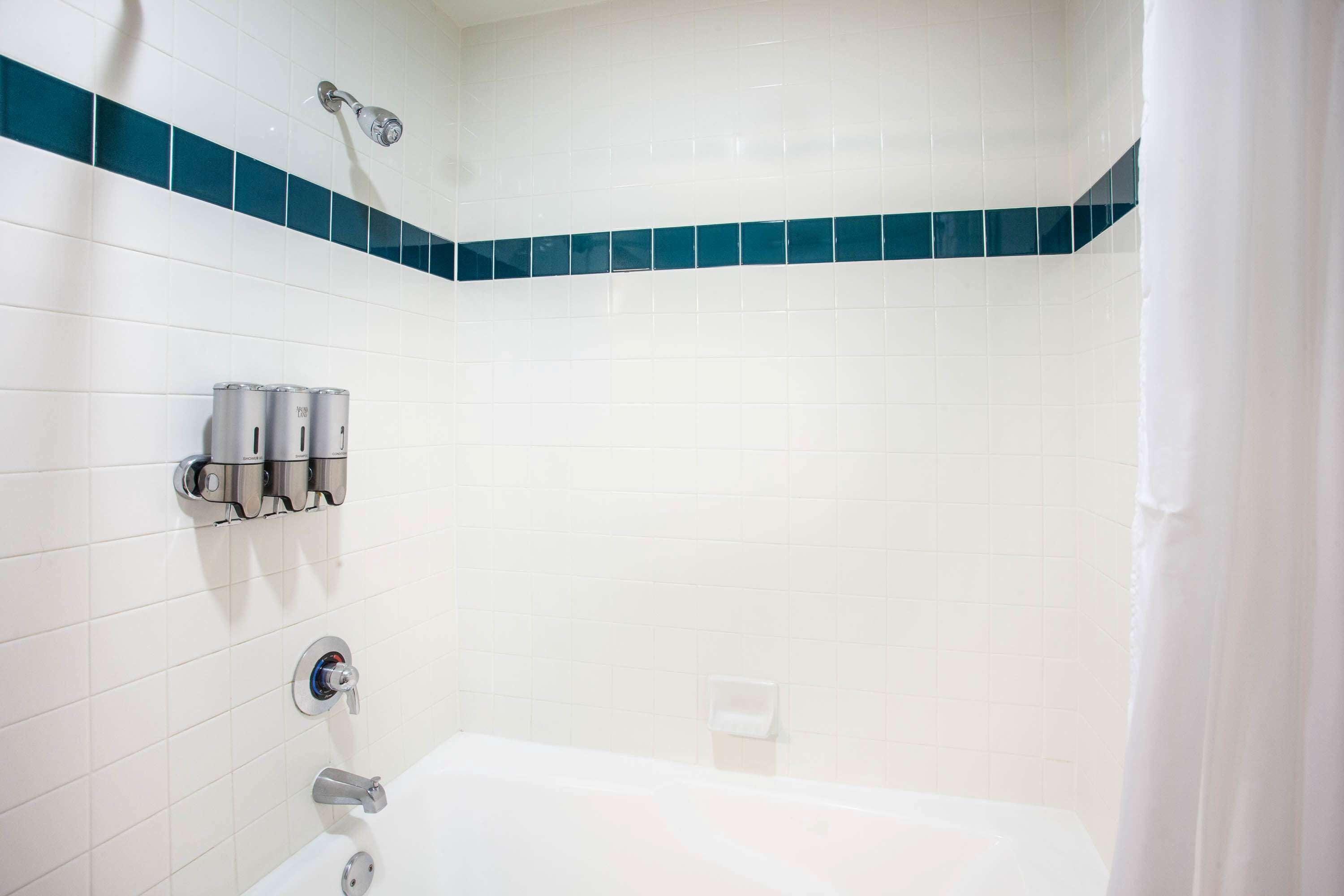 Un baño con azulejos blancos, una bañera, un cabezal de ducha y un dispensador de toallas.