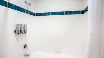 Een badkamer met witte tegels, een bad, een douchekop en een handdoekdispenser.