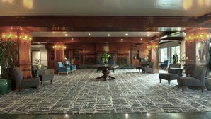 A lobby with a patterned carpet, wooden furniture, and a central table with a vase.
