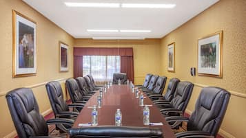 A conference room with a long table, leather chairs, water bottles, framed pictures on the walls, and a large window with curtains.