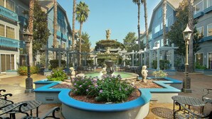A courtyard with a central fountain, surrounded by benches and palm trees.