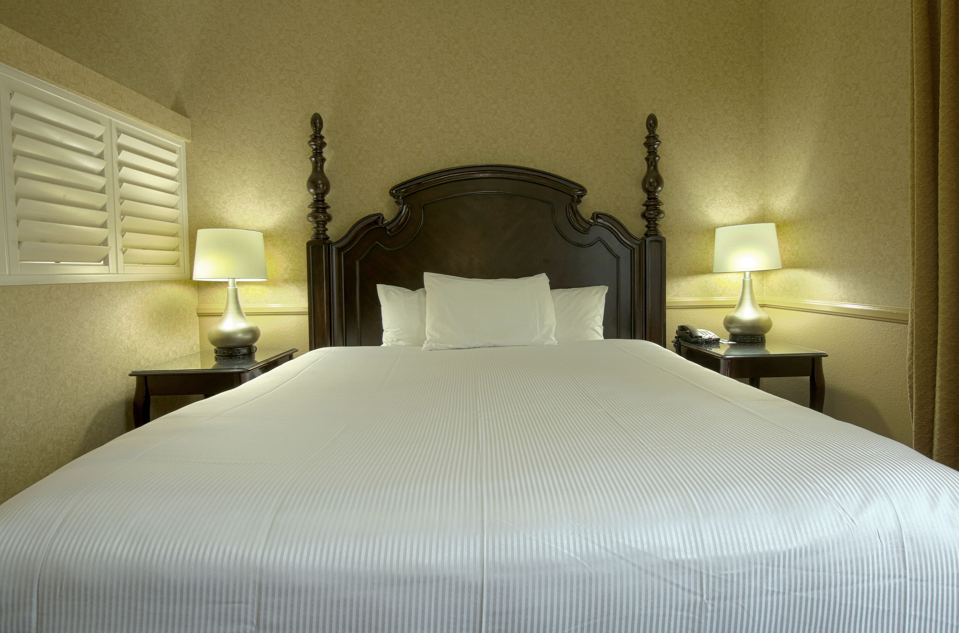 A neatly made bed with white linens, two bedside tables with lamps, and a wooden headboard.