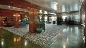 A spacious lobby with a polished floor, wooden furniture, and a large potted plant.