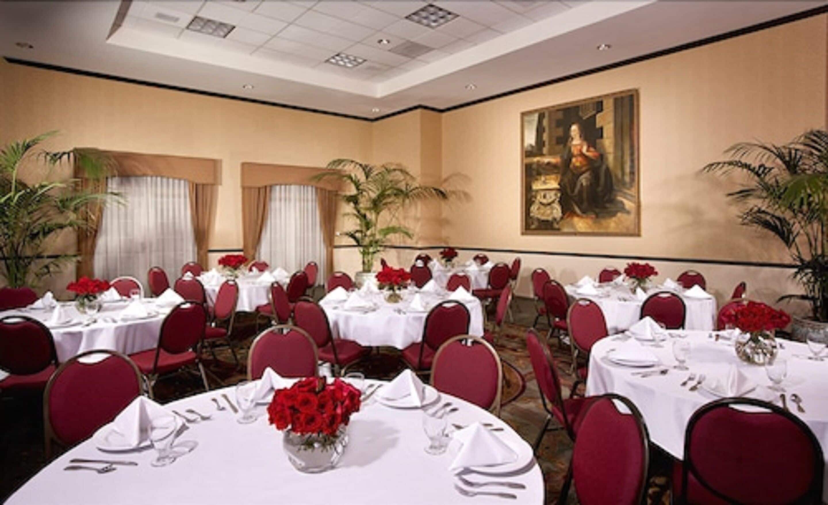 Un salón de banquetes con mesas redondas, sillas rojas y manteles blancos.