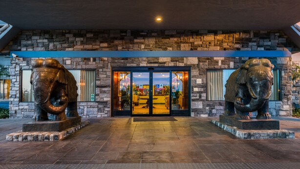 A stone facade with a large entrance, two elephant statues, and a view of the interior through the glass doors.