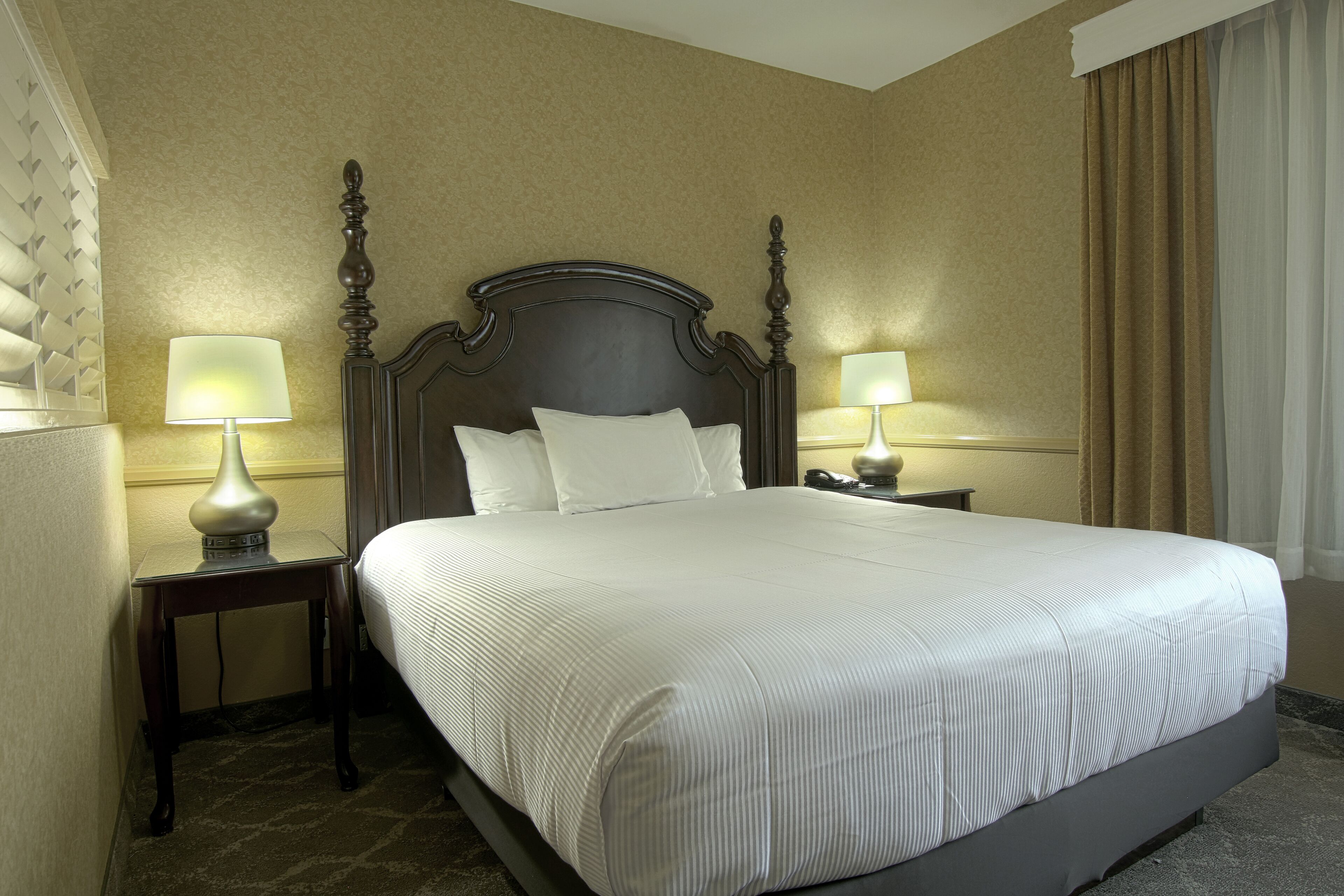 Une chambre d’hôtel avec un grand lit, deux tables de chevet avec des lampes et une fenêtre avec des rideaux.