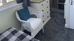 A room with a white wicker chair, a dresser with a mirror, a flat-screen TV, and a walk-in closet. - Green Apple Bed and Breakfast (St Ives)