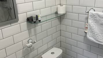 A bathroom with white tiles, a glass shelf with toiletries, a toilet, and a sink.