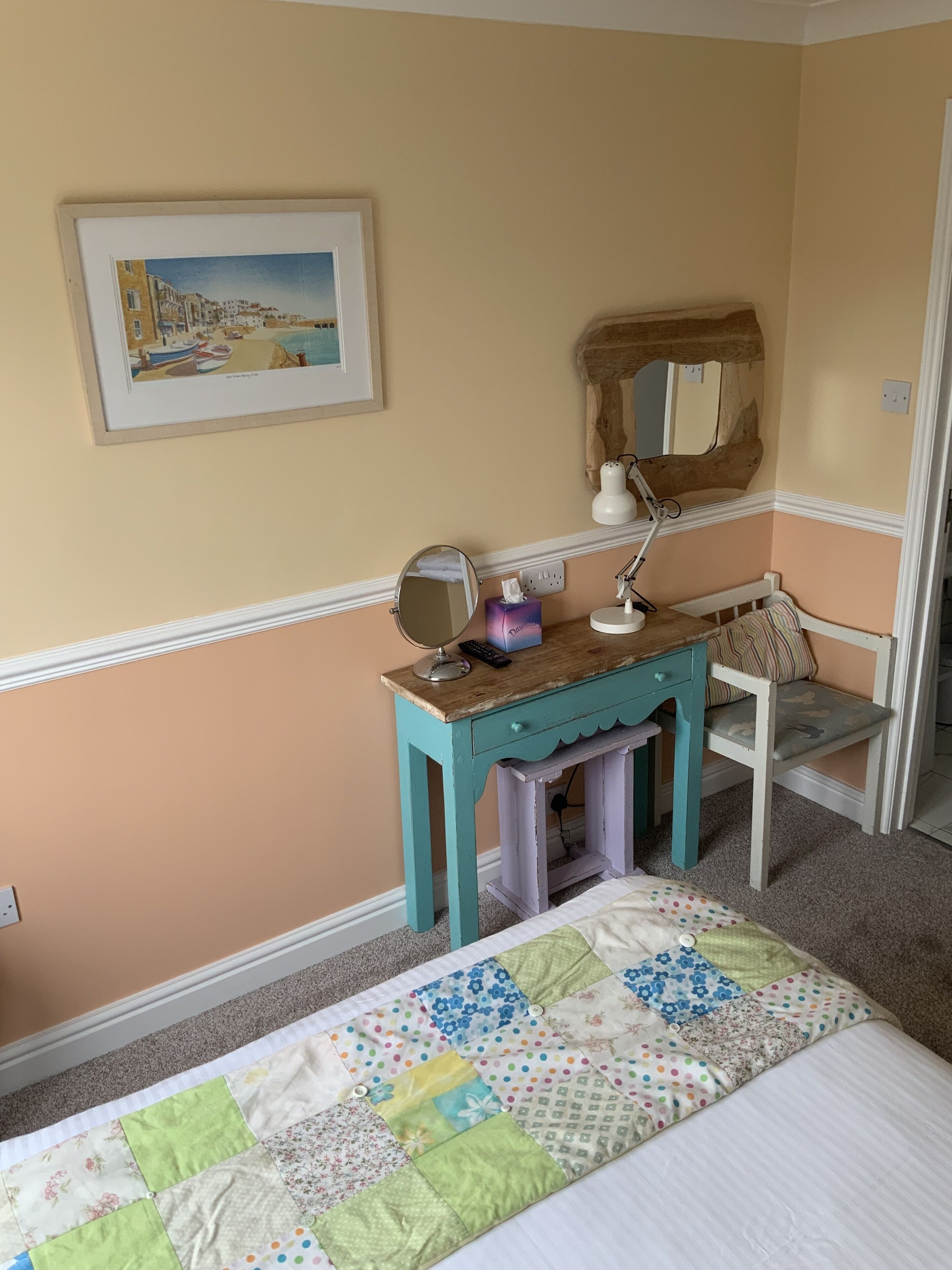 A bedroom with a bed, a desk with a mirror, a chair, and a framed picture on the wall.