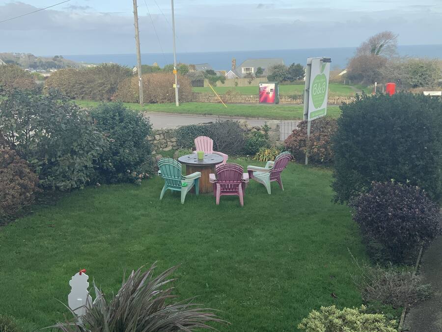 A grassy outdoor area with a table and chairs, a flag, and a view of the sea.