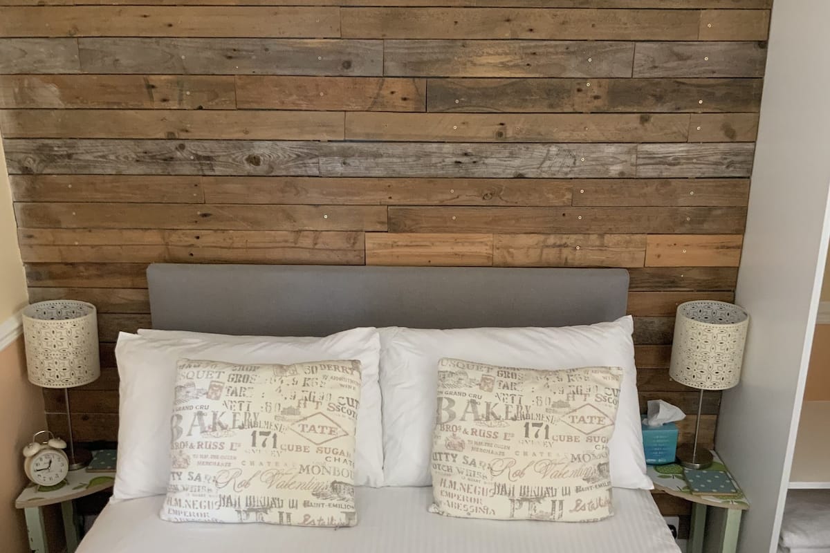 Una cama con dos almohadas, un cabecero de madera y dos mesitas de noche con lámparas.