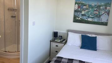 A bedroom with a bed, a nightstand, a painting, and a glass shower enclosure.