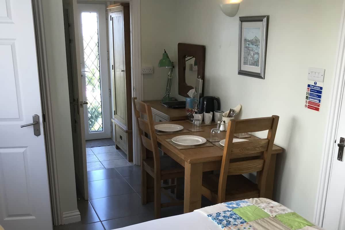 Una habitación con una cama, una mesa de comedor con sillas, una pequeña cocina y una puerta que da a un balcón.