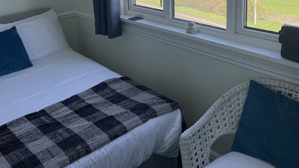 A bedroom with two beds, a large window with a view of the sea and landscape, and a painting on the wall. - Green Apple Bed and Breakfast (St Ives)