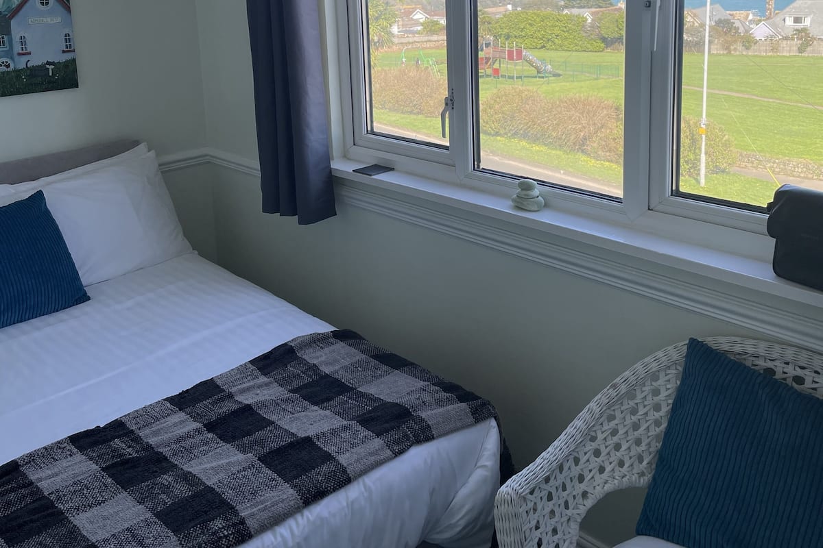 Un dormitorio con dos camas, un ventanal con vistas al mar y al paisaje, y un cuadro en la pared.
